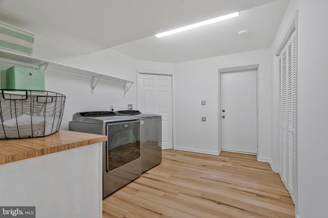 clothes washing area with light wood-style floors, laundry area, baseboards, and washing machine and clothes dryer