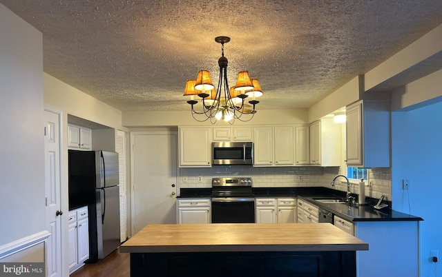 kitchen featuring a notable chandelier, stainless steel appliances, white cabinets, a sink, and wood counters