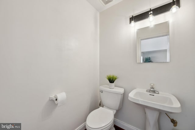 half bath featuring baseboards, visible vents, a sink, and toilet