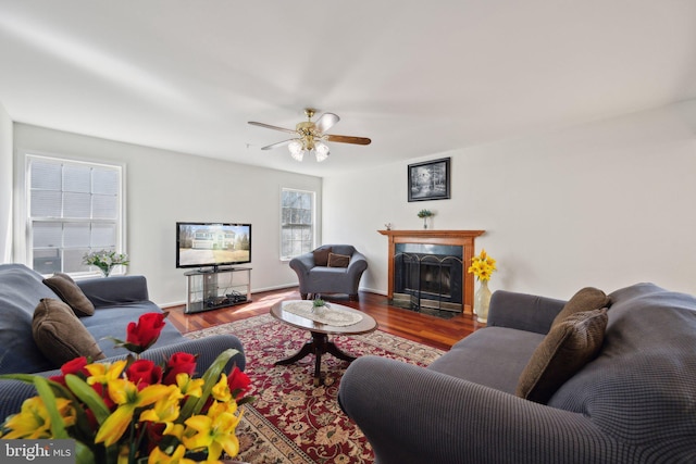 living area with a fireplace with flush hearth, ceiling fan, baseboards, and wood finished floors