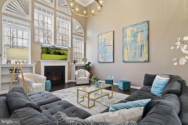 living room with a glass covered fireplace, wood finished floors, a high ceiling, baseboards, and a chandelier