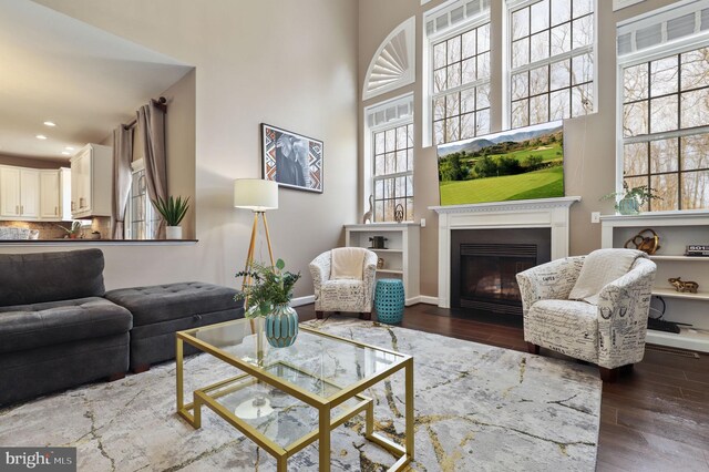 living room with recessed lighting, a fireplace with flush hearth, dark wood-type flooring, and a towering ceiling