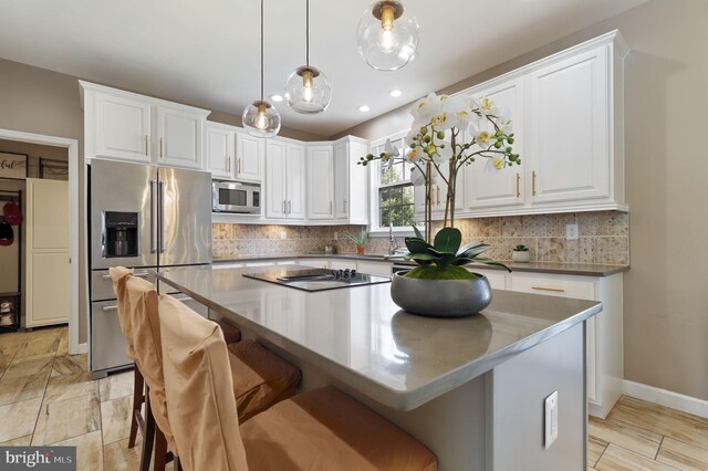 kitchen featuring decorative backsplash, white cabinets, appliances with stainless steel finishes, a kitchen bar, and a center island