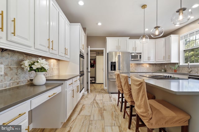 kitchen with backsplash, decorative light fixtures, a kitchen bar, white cabinets, and stainless steel appliances