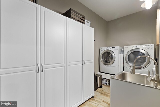 clothes washing area with cabinet space, washing machine and dryer, and light wood-type flooring