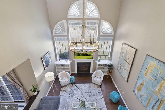 living room with baseboards, a fireplace, a high ceiling, an inviting chandelier, and wood finished floors