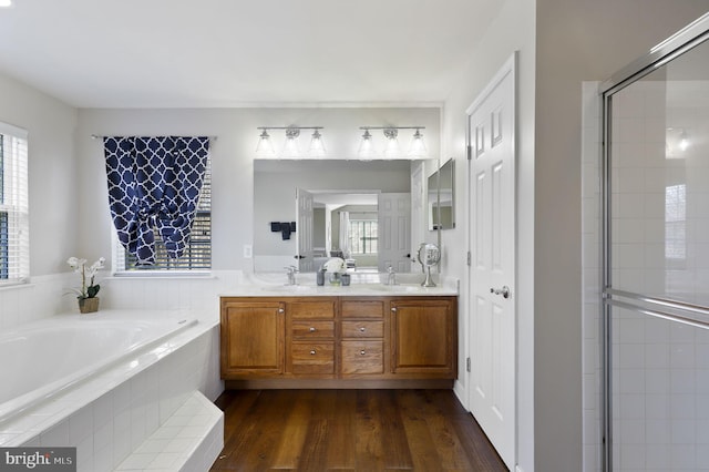 full bath with double vanity, a tile shower, wood finished floors, a bath, and a sink