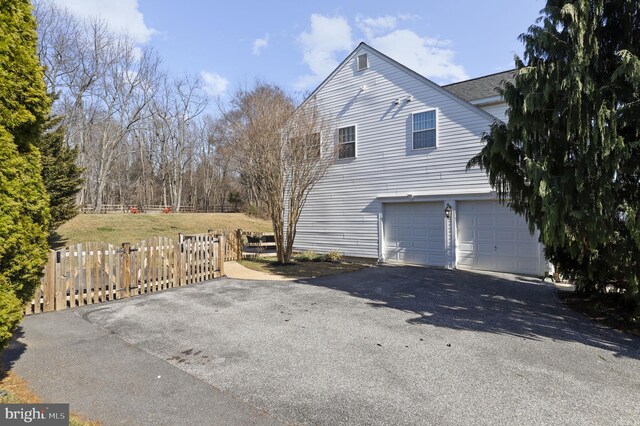 view of side of property featuring an attached garage, fence, and driveway