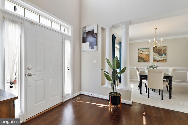 foyer entrance featuring visible vents, crown molding, decorative columns, a chandelier, and dark wood-style flooring