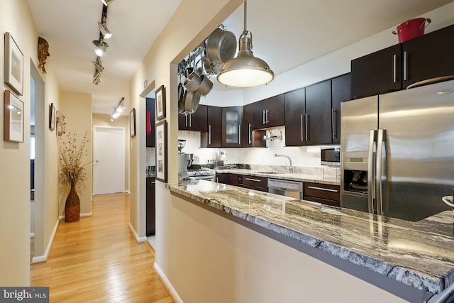 kitchen with light wood finished floors, dark brown cabinetry, light stone counters, appliances with stainless steel finishes, and a sink