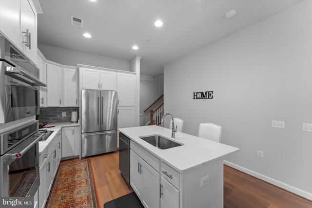 kitchen with stainless steel appliances, a sink, visible vents, backsplash, and dark wood-style floors