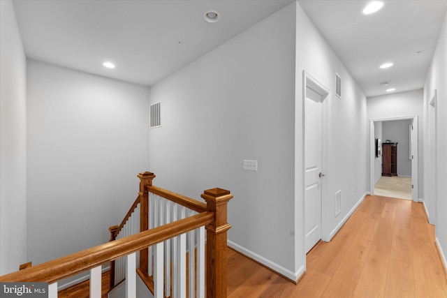 hall with light wood finished floors, recessed lighting, visible vents, and an upstairs landing