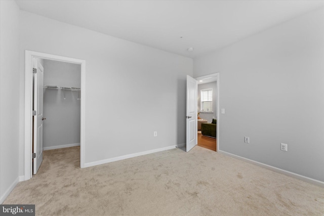 unfurnished bedroom with a closet, baseboards, a walk in closet, and carpet flooring