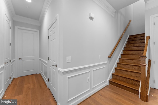 stairs with a wainscoted wall, crown molding, a decorative wall, and wood finished floors