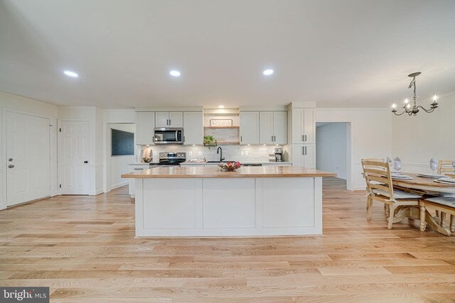 kitchen with a sink, a kitchen island, appliances with stainless steel finishes, light wood finished floors, and decorative backsplash