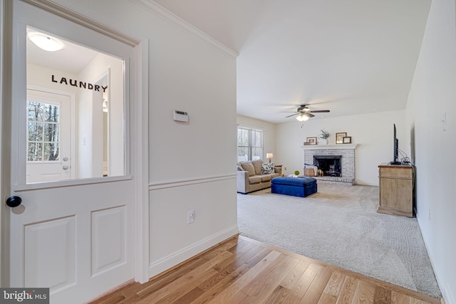 foyer entrance featuring a brick fireplace, baseboards, ceiling fan, ornamental molding, and wood finished floors