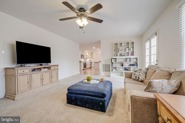 living area with built in features, light colored carpet, and ceiling fan