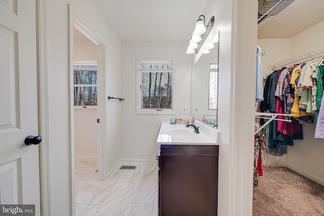 bathroom featuring a walk in closet, baseboards, marble finish floor, and vanity