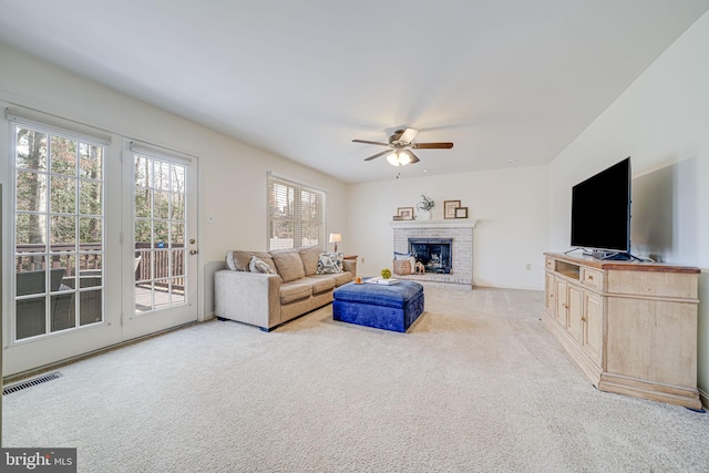 living room with ceiling fan, a fireplace, visible vents, and light carpet