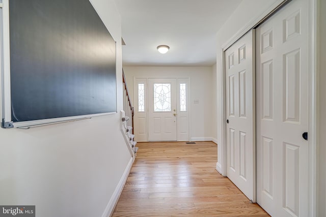 entryway with stairway, light wood-style floors, and baseboards