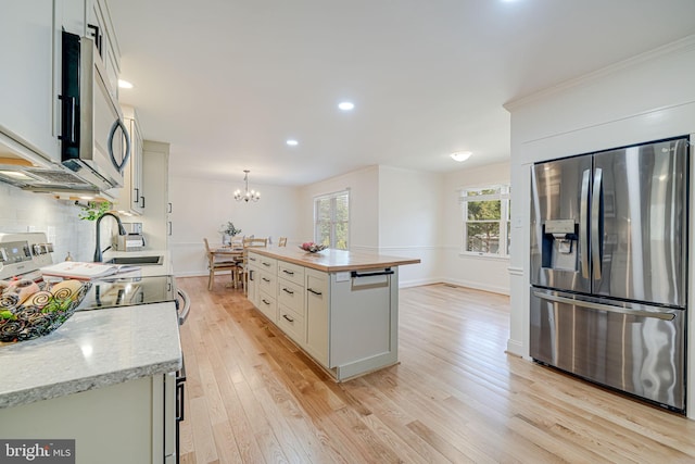 kitchen with tasteful backsplash, light wood-style flooring, appliances with stainless steel finishes, a notable chandelier, and a sink