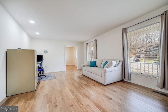 living room with light wood finished floors, visible vents, a healthy amount of sunlight, and baseboards