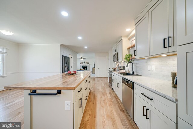 kitchen with a kitchen island, butcher block counters, light wood-type flooring, appliances with stainless steel finishes, and a sink