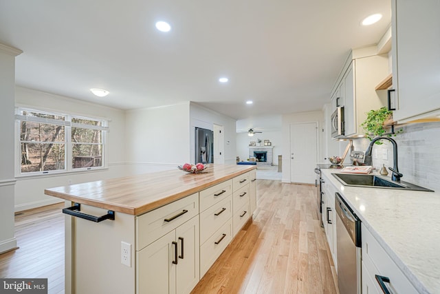 kitchen with butcher block countertops, light wood-style flooring, a sink, appliances with stainless steel finishes, and a fireplace