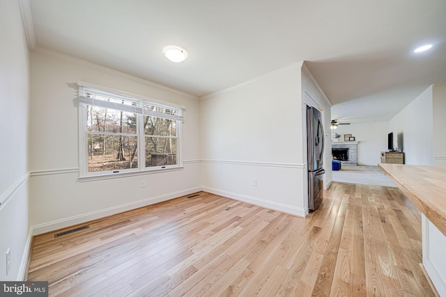 unfurnished room with visible vents, a brick fireplace, light wood-style floors, and ornamental molding