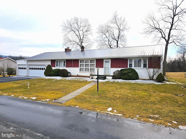 ranch-style house featuring metal roof, a garage, driveway, a front lawn, and a chimney