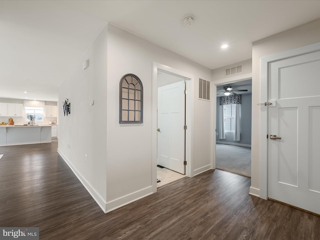 corridor featuring visible vents, baseboards, and dark wood-style floors