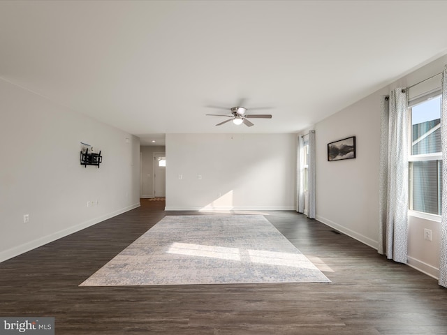 unfurnished living room featuring dark wood-type flooring, baseboards, and ceiling fan