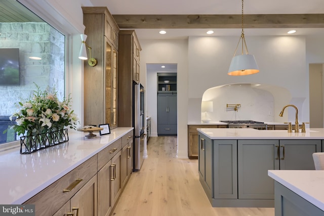 kitchen with light wood finished floors, beamed ceiling, hanging light fixtures, stainless steel appliances, and a sink