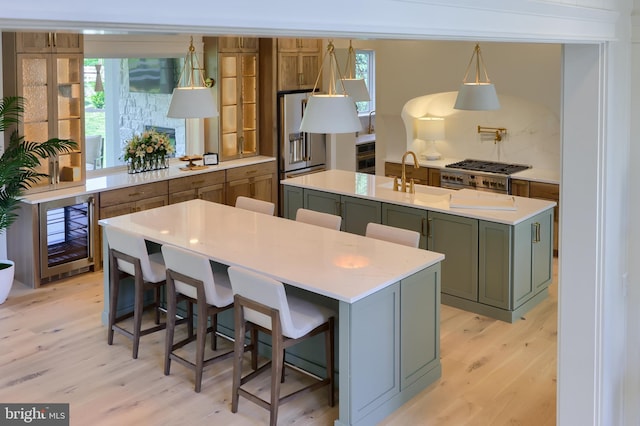 kitchen featuring a sink, light countertops, a wealth of natural light, light wood finished floors, and a center island with sink