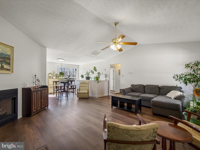 living room featuring dark wood-style floors, a fireplace, lofted ceiling, visible vents, and a textured ceiling