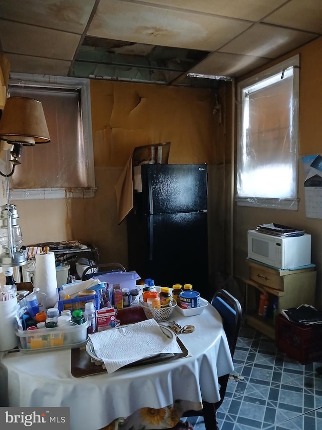 kitchen featuring white microwave, a drop ceiling, and freestanding refrigerator