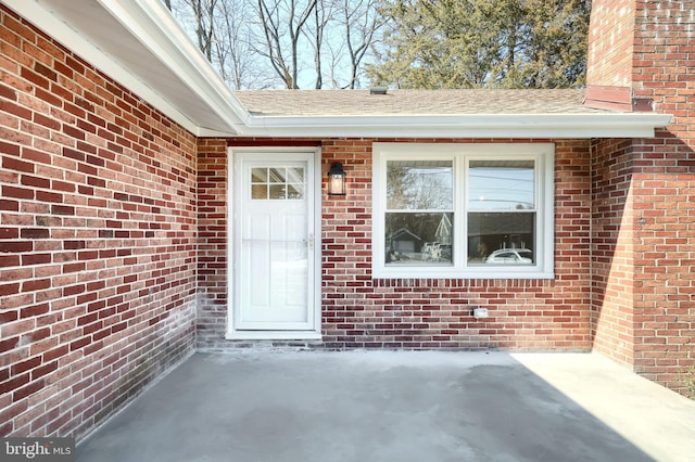 view of exterior entry featuring brick siding and roof with shingles