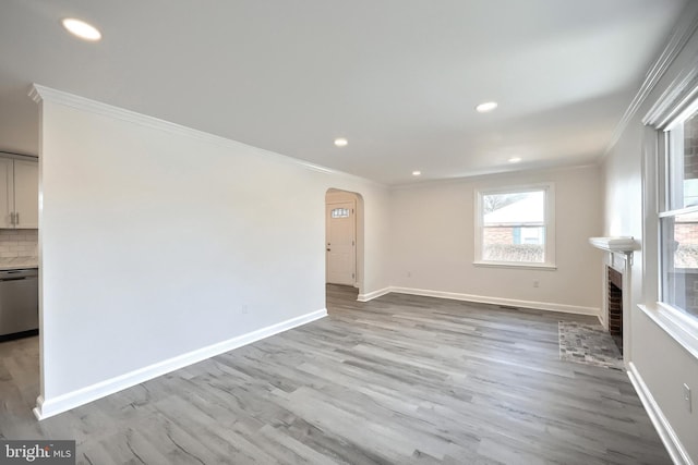 unfurnished living room featuring baseboards, arched walkways, ornamental molding, wood finished floors, and a brick fireplace