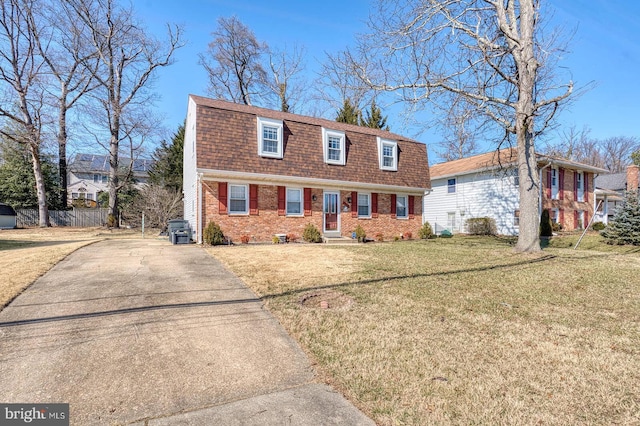 colonial inspired home with brick siding, a shingled roof, a gambrel roof, driveway, and a front lawn