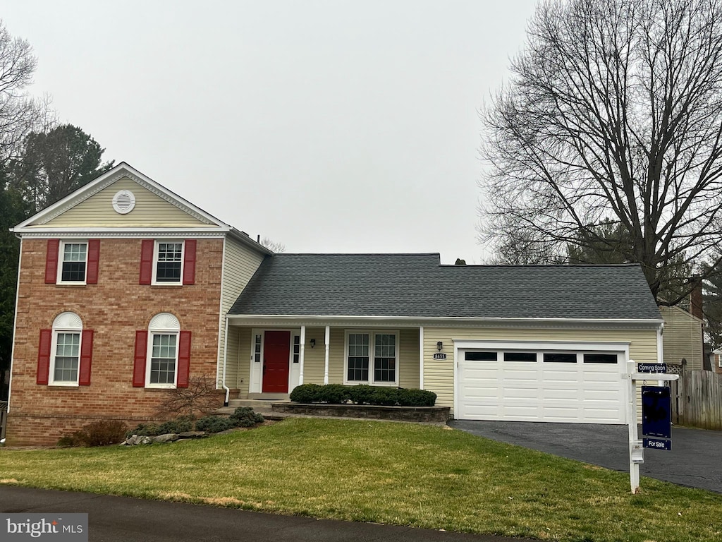 traditional-style home with a shingled roof, a front lawn, a garage, aphalt driveway, and brick siding