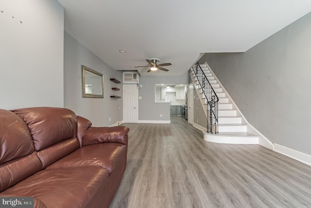 living area featuring stairs, light wood finished floors, a ceiling fan, and baseboards