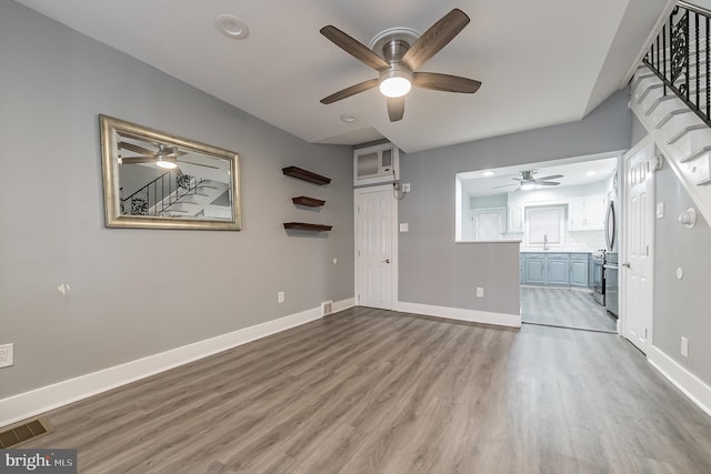 unfurnished living room featuring stairway, baseboards, visible vents, and wood finished floors