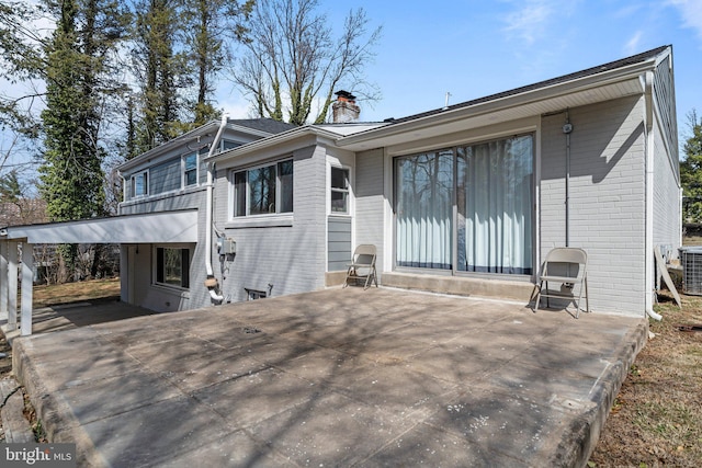 rear view of property featuring brick siding, a patio area, an attached carport, and a chimney