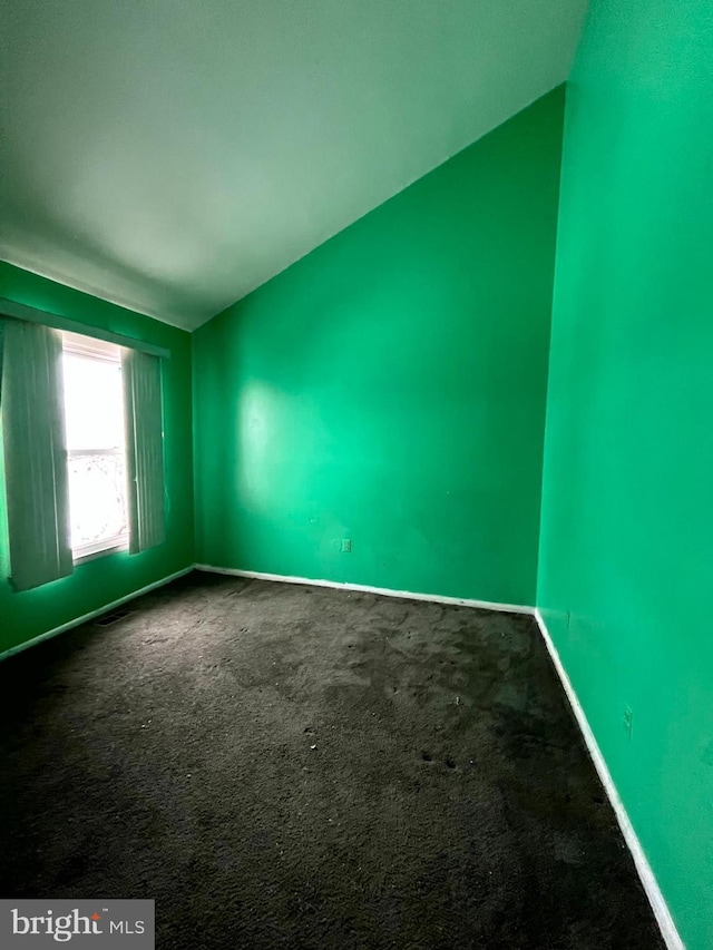 empty room featuring baseboards, dark carpet, and vaulted ceiling