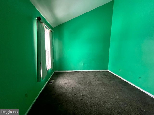 spare room featuring lofted ceiling, dark carpet, visible vents, and baseboards