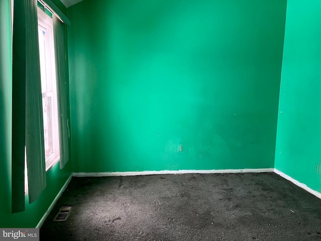 unfurnished room featuring a wealth of natural light, dark carpet, visible vents, and baseboards