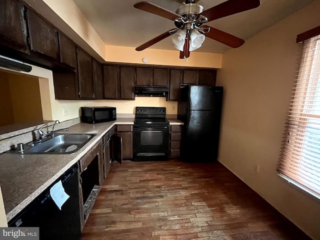 kitchen featuring under cabinet range hood, a sink, dark brown cabinets, dark wood-style floors, and black appliances