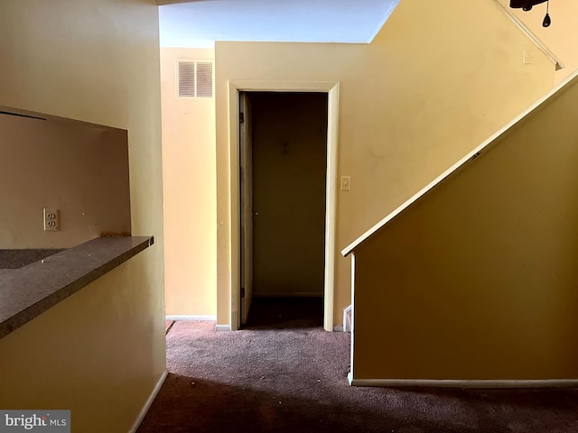 hallway featuring baseboards, visible vents, and dark carpet