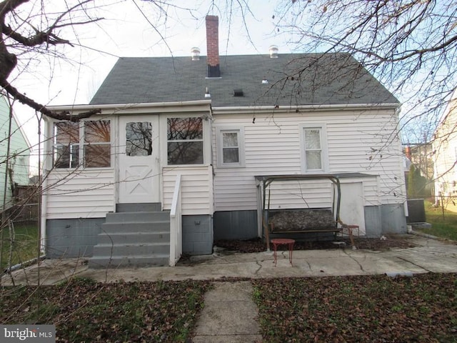 rear view of house featuring entry steps, a patio area, a shingled roof, and a chimney