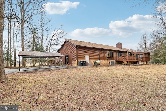 rear view of property featuring a chimney, a lawn, central AC, stone siding, and a wooden deck